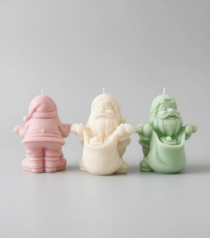 Three ceramic Santa Claus figures on a wooden table with a festive background including a Christmas tree and decorations.